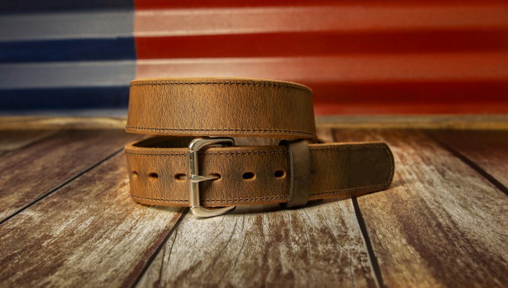 Brown leather belt with a metal buckle lying on a wooden floor