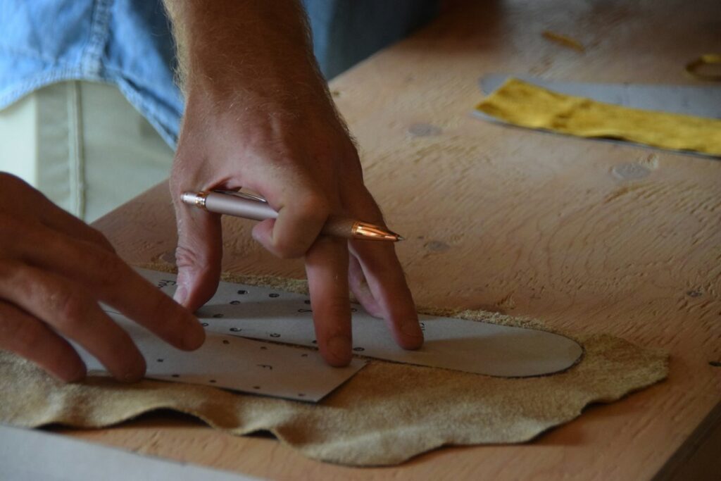Hands tracing a pattern onto a piece of tan leather before cutting